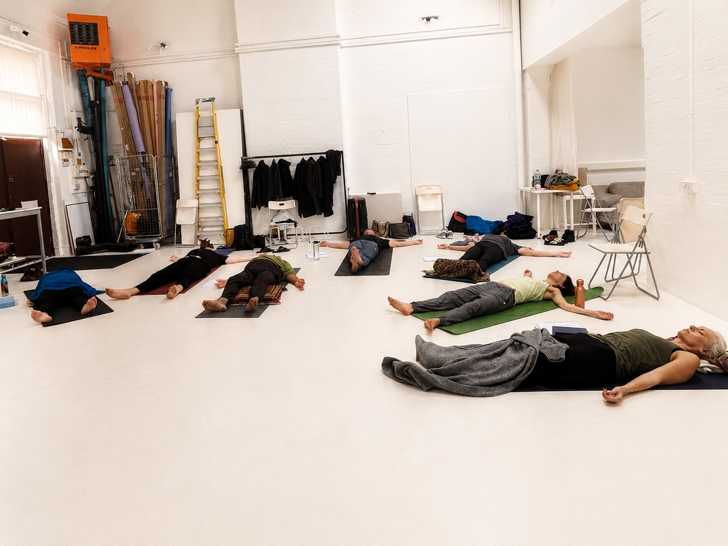 Students lying down in relaxation during Kundalini GlobalTeacher Training in a bright white London studio.